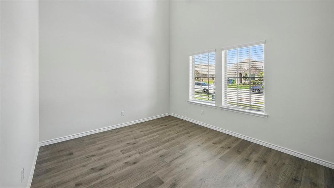 Room with wood-finish flooring, two large windows with blinds, white walls, and high ceilings