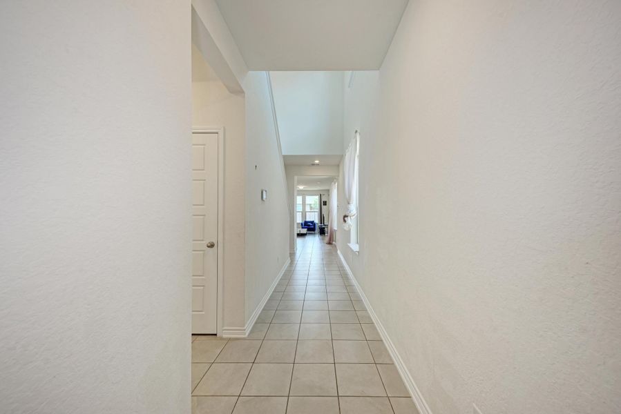 A long, bright hallway features sleek tile flooring leading toward an inviting open living area.