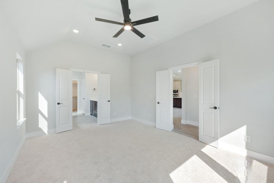 Empty bedroom with carpet, ceiling fan, and two open doorways leading to closet and bathroom