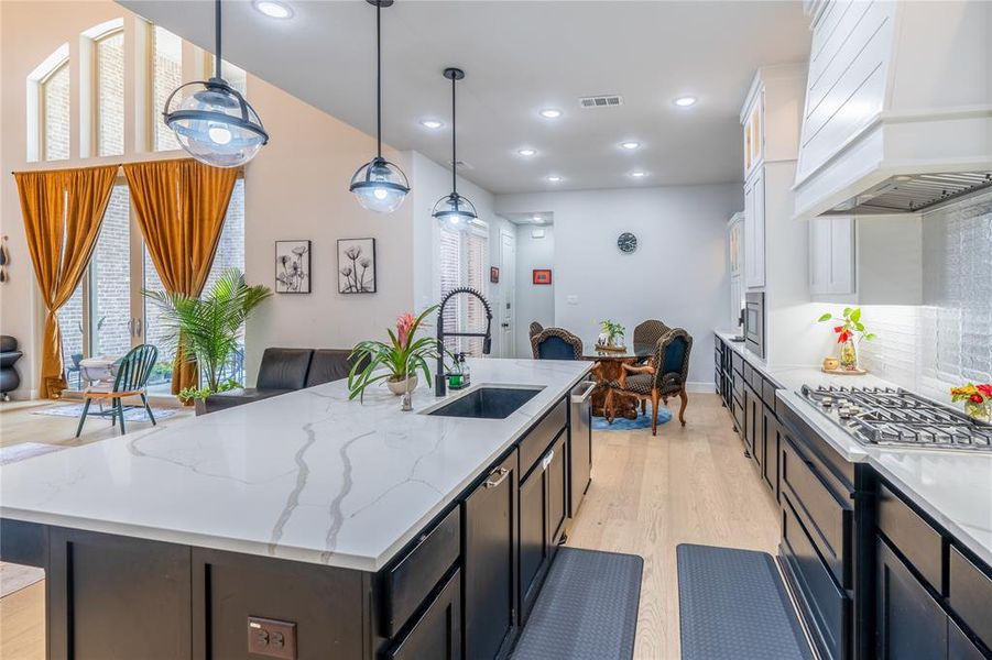 Kitchen featuring open floor plan, decorative light fixtures, light wood-style floors, a center island with sink, and custom range hood