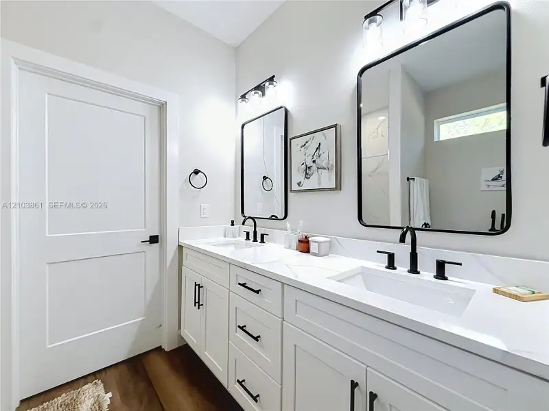 Dual-sink vanity featuring white cabinetry, solid-surface countertops, black hardware, and rectangular under-mount basins paired with black wall-mounted mirrors and matching light fixtures