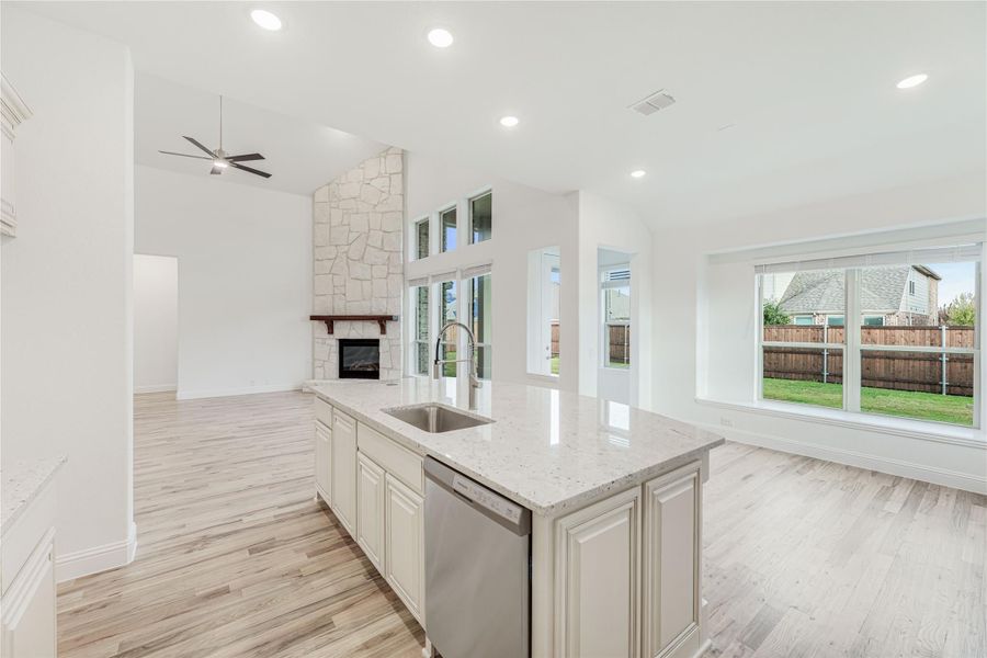 Kitchen island with sink and quartz countertop open to living room with stone fireplace and light wood floors