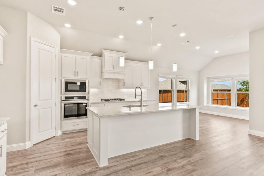 Kitchen with white cabinets, large center island, stainless steel appliances, and light wood floors Kitchen with white cabinets, large center island, stainless steel appliances, and light wood floors