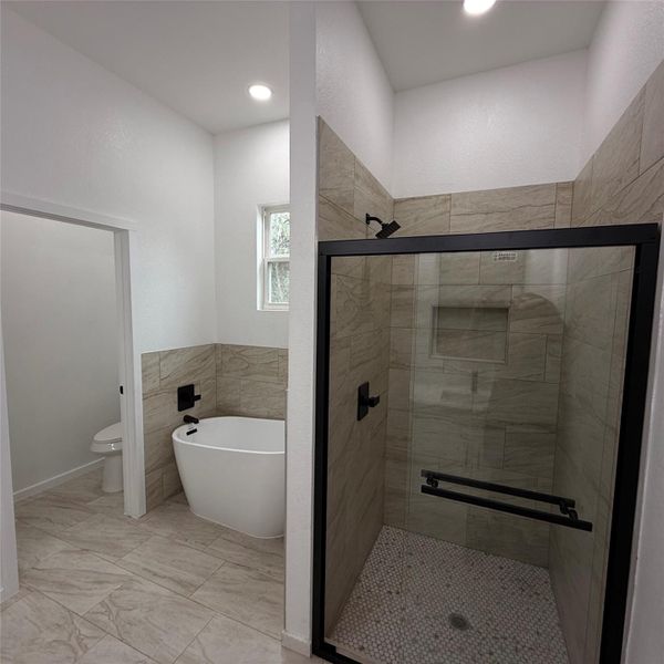 Contemporary bathroom featuring a freestanding soaking tub, a tiled walk-in shower with a glass enclosure, matte black fixtures, recessed lighting, and wood-finish tile flooring