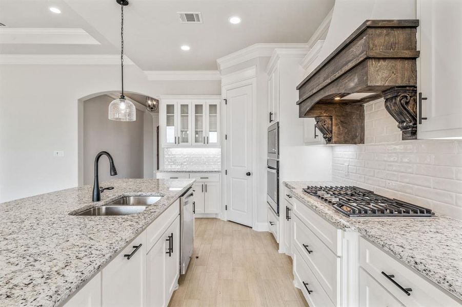 Kitchen with ornamental molding, hanging light fixtures, white cabinetry, glass insert cabinets, and decorative backsplash