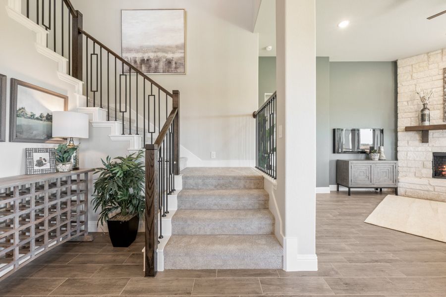 Carpeted staircase with dark metal balusters and wood handrail, open to living room with stone fireplace