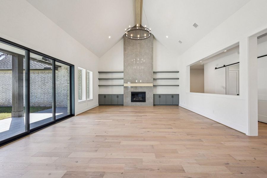 This living room features high ceilings and a modern, minimalist design. It includes a large stone fireplace, ample natural light from floor-to-ceiling windows, and sleek, neutral furnishings. Ideal for a contemporary lifestyle.