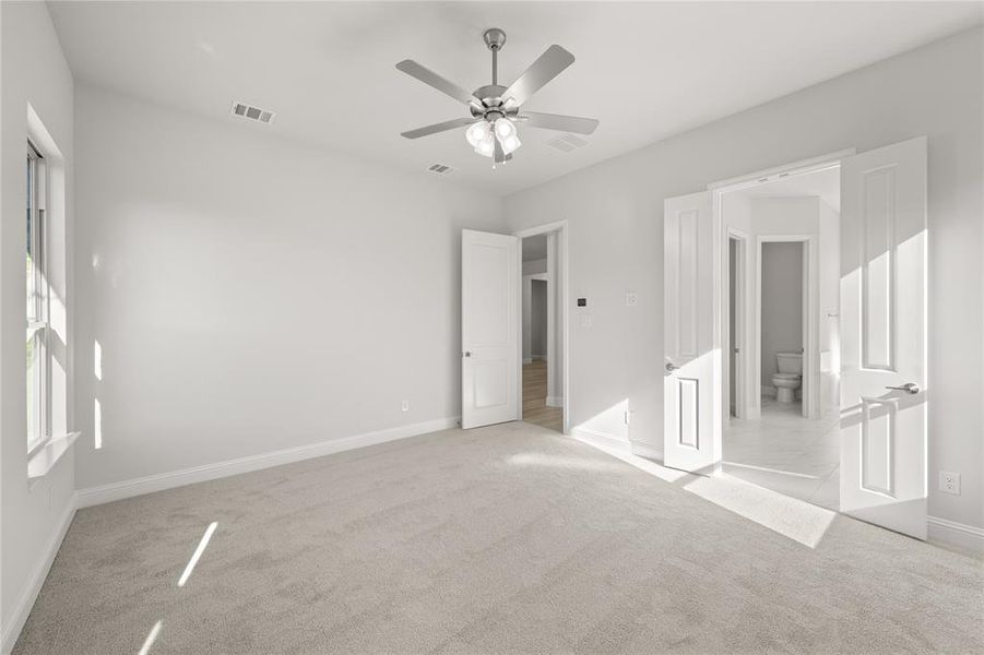 Primary Bedroom featuring ensuite bath, ceiling fan, and light colored carpet