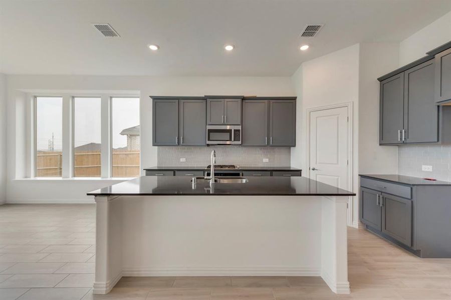 Kitchen with light hardwood / wood-style floors, gray cabinets, a kitchen island with sink, sink, and tasteful backsplash