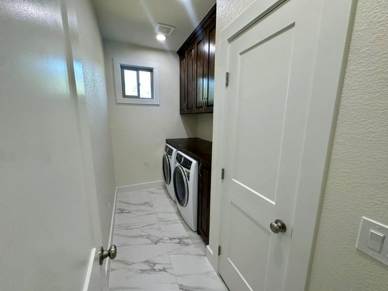 Washroom featuring a textured wall, cabinet space, light marble finish floors, and washing machine and dryer