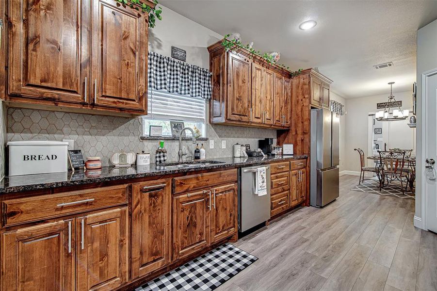 Kitchen with sink, light hardwood / wood-style flooring, dark stone countertops, decorative light fixtures, and stainless steel appliances