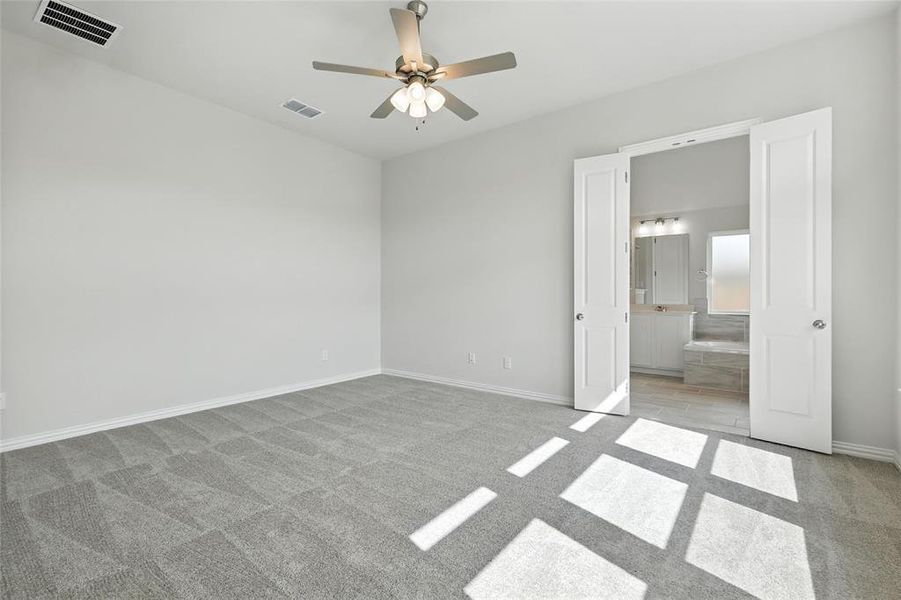 Unfurnished bedroom with light carpet, ensuite bathroom, and a ceiling fan