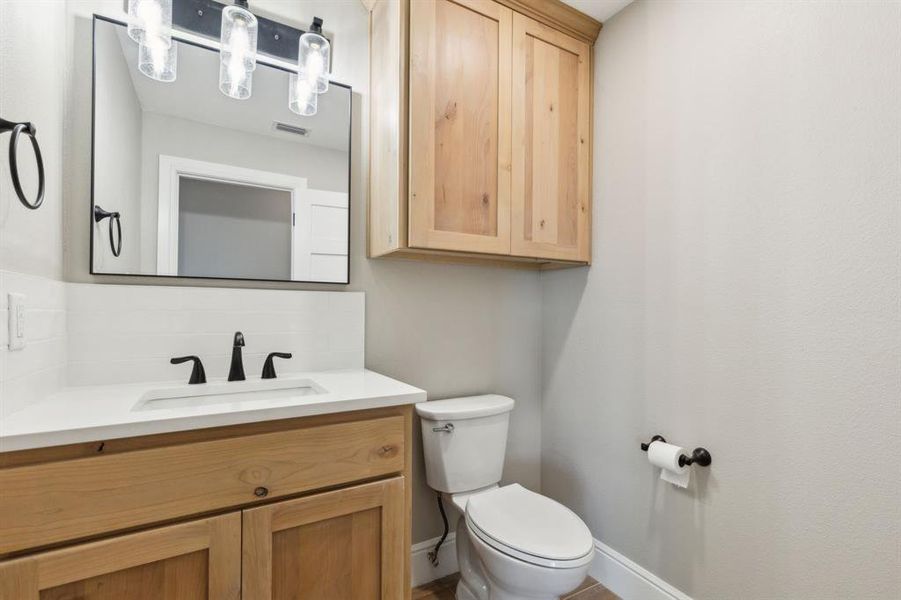 Half bathroom featuring commode, vanity, storage and light fixture. Half bathroom featuring commode, vanity, storage and light fixture.