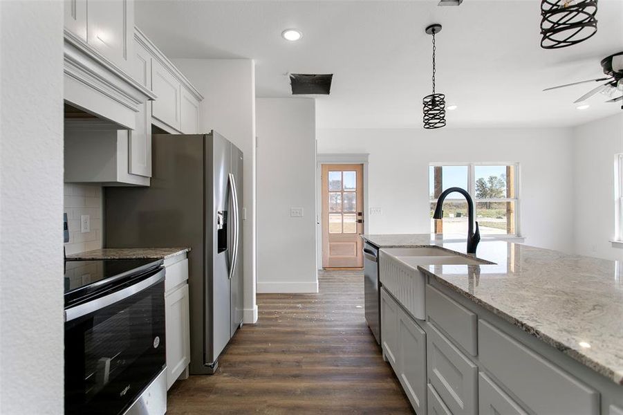 Kitchen featuring light stone countertops, backsplash, stainless steel appliances, dark wood-type flooring, and white cabinetry