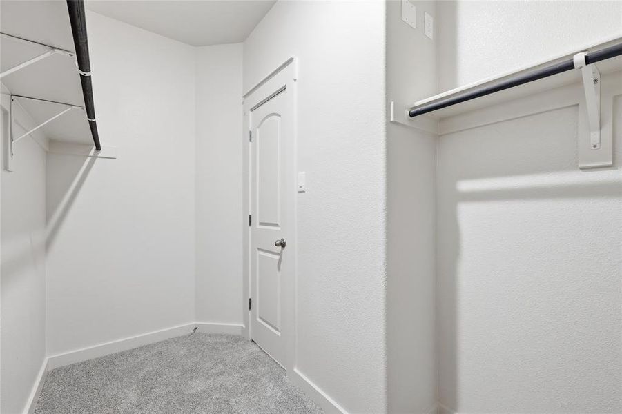 Walk-in closet featuring light grey carpet flooring, white walls, and built-in white shelving with black hanging rods Walk-in closet featuring light grey carpet flooring, white walls, and built-in white shelving with black hanging rods