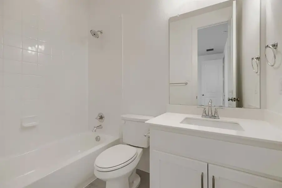 Bathroom featuring a white bathtub with subway tile surround, polished chrome fixtures, a white vanity with an integrated sink, and a large wall-mounted mirror
