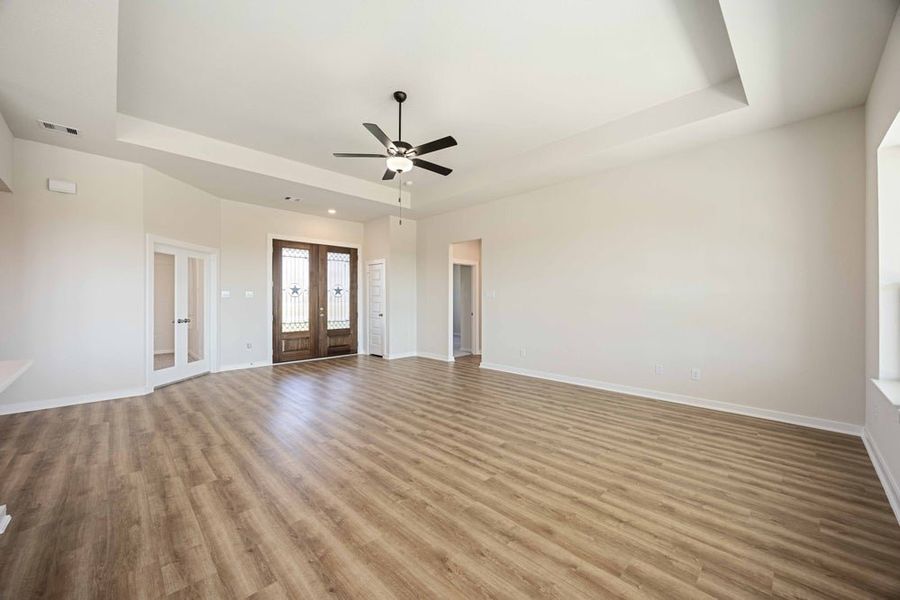 Empty living room with wood-look flooring, tray ceiling, ceiling fan, and double front doors