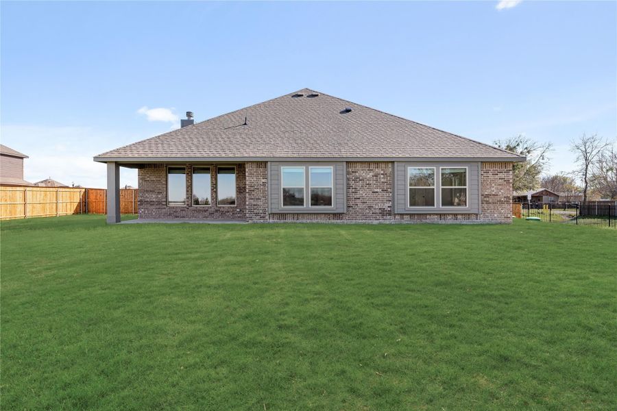 Rear view of single-story brick home with hip roof, covered patio, and large fenced backyard Rear view of single-story brick home with hip roof, covered patio, and large fenced backyard
