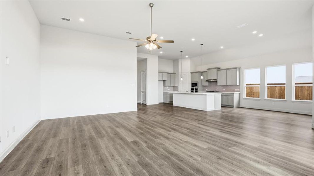 Open-concept living area featuring wood-finish flooring, a contemporary kitchen with a large island, stainless steel appliances, pendant lighting, and multiple windows