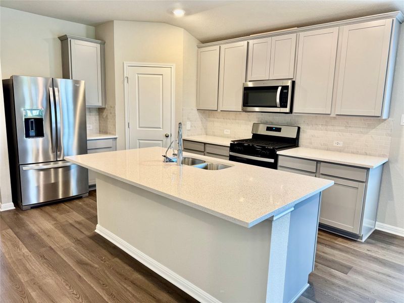 Kitchen with stainless steel appliances, wood finished floors, backsplash, a center island with sink, and lofted ceiling