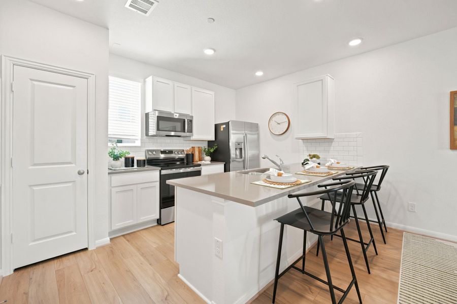 Recessed lighting and a central breakfast island define this modern culinary workspace with wood-style flooring.