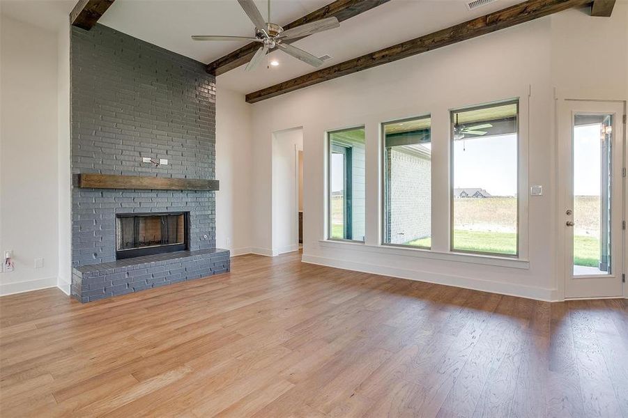 Unfurnished living room featuring beam ceiling, ceiling fan, light hardwood / wood-style flooring, and a fireplace