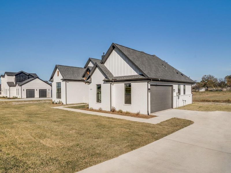 View of front of house featuring a shingled roof, a front yard, brick siding, and concrete driveway