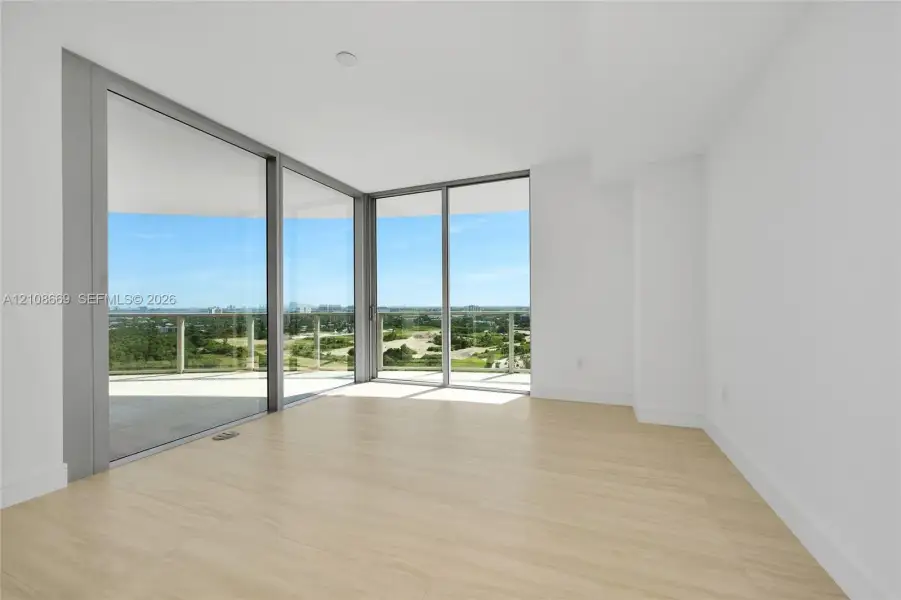 Floor-to-ceiling glass walls, wrap-around balcony with glass railings, neutral large-format tile flooring, and crisp white wall finishes