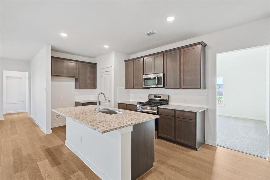 Kitchen with light hardwood / wood-style flooring, an island with sink, stainless steel appliances, sink, and light stone counters