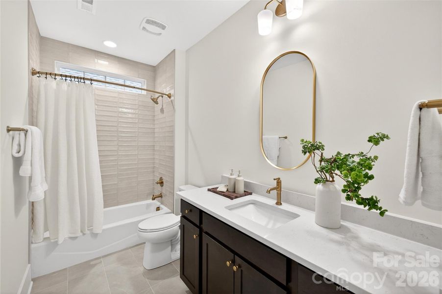 Bathroom #2 showcases tile to the ceiling, a transom window for natural light and a framed mirror with quartz countertops.