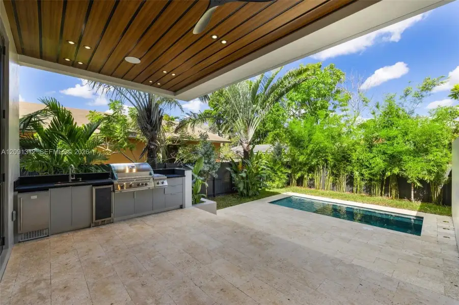 Covered outdoor kitchen featuring built-in cabinetry, stainless steel appliances, and a wood-slat ceiling with recessed lighting Covered outdoor kitchen featuring built-in cabinetry, stainless steel appliances, and a wood-slat ceiling with recessed lighting