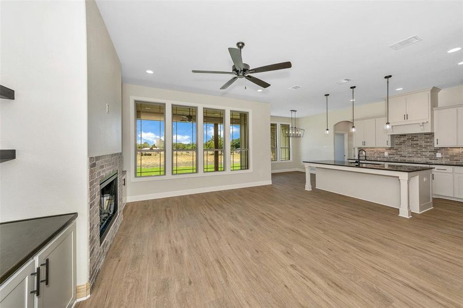 Unfurnished living room with sink, ceiling fan, a brick fireplace, and light hardwood / wood-style flooring