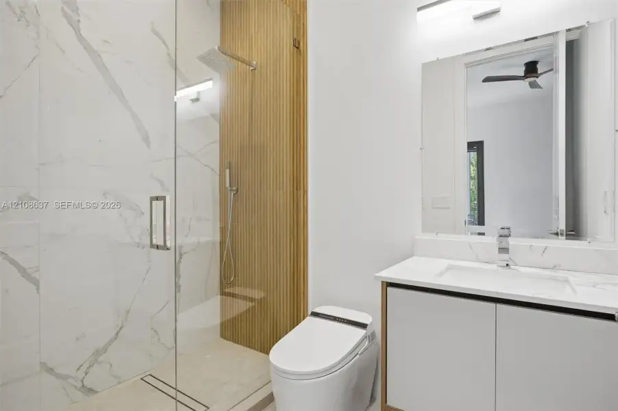 Walk-in shower with floor-to-ceiling stone-patterned tile, vertical wood-slat accent wall, rainfall showerhead, glass enclosure, and floating vanity with integrated countertop and sink