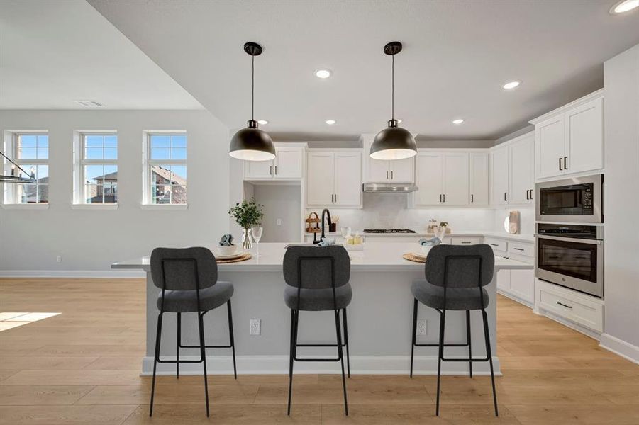 Kitchen with white cabinetry, stainless steel appliances, an island with sink, light wood-style floors, and hanging light fixtures