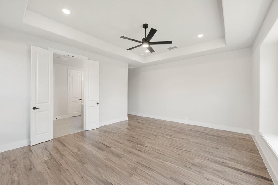 Empty bedroom with tray ceiling, black ceiling fan, and light hardwood floors