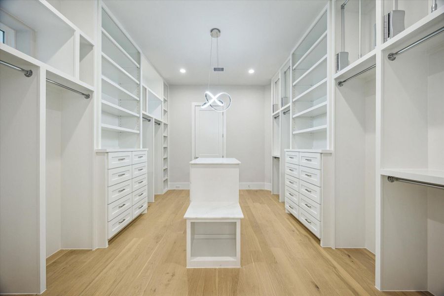 One of the primary closets - offers a marble-topped island with built-in storage. The closet offers drawers, shelves, and stainless steel hanging rods. The closet has access to the utility room. One of the primary closets - offers a marble-topped island with built-in storage. The closet offers drawers, shelves, and stainless steel hanging rods. The closet has access to the utility room.