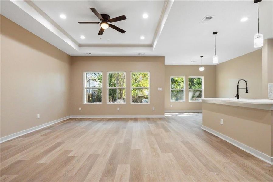 Unfurnished living room with light wood-type flooring, a tray ceiling, sink, and ceiling fan