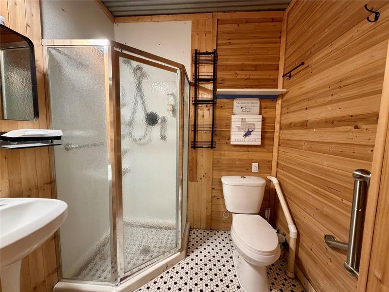 A compact bathroom offers functionality with a corner shower and a single vanity, all complemented by rustic wood paneling.