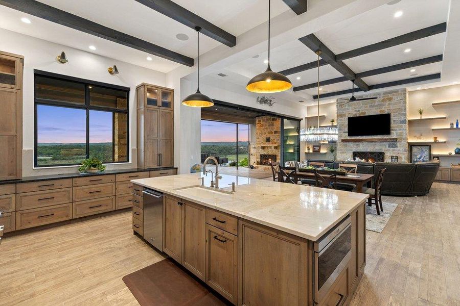 Gourmet kitchen with a large central island, light wood-finish cabinetry, built-in appliances, and a window overlooking a natural landscape