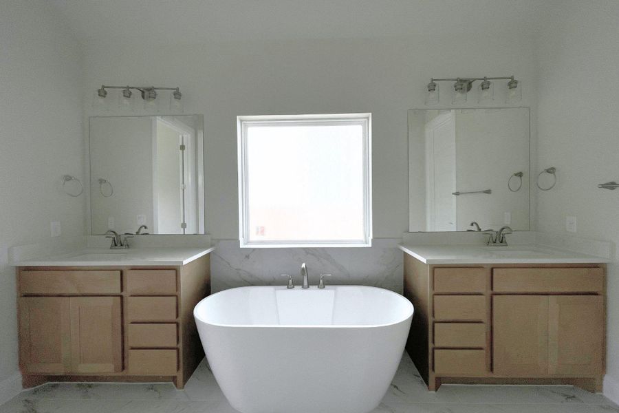 A well-appointed primary bathroom showcases a freestanding tub, framed by dual vanities and illuminated by a central window.