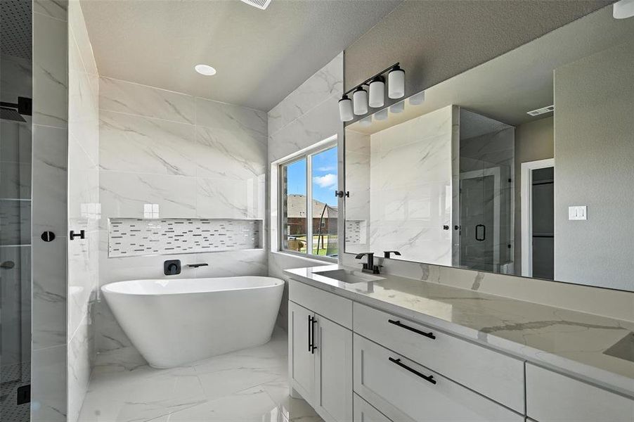 Full bath featuring marble tiled flooring, vanity, a marble finish shower, a freestanding bath, and tile walls Full bath featuring marble tiled flooring, vanity, a marble finish shower, a freestanding bath, and tile walls
