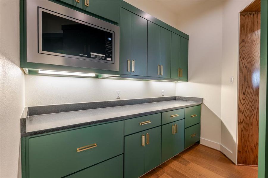 Kitchen with green cabinets, stainless steel microwave, and light wood-style flooring