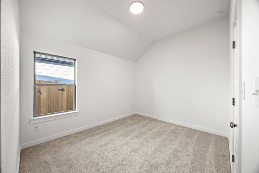 A window-lit room features soft carpet and a vaulted ceiling, offering a comfortable, neutral retreat.