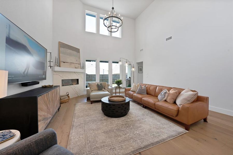 Living area featuring high ceilings, wood-finish flooring, a linear electric fireplace with a decorative stone surround, and large windows with transoms Living area featuring high ceilings, wood-finish flooring, a linear electric fireplace with a decorative stone surround, and large windows with transoms