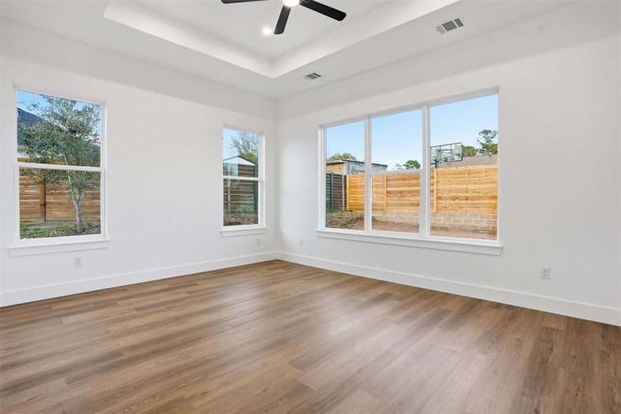 Empty room with ceiling fan, dark wood-style floors, and a raised ceiling