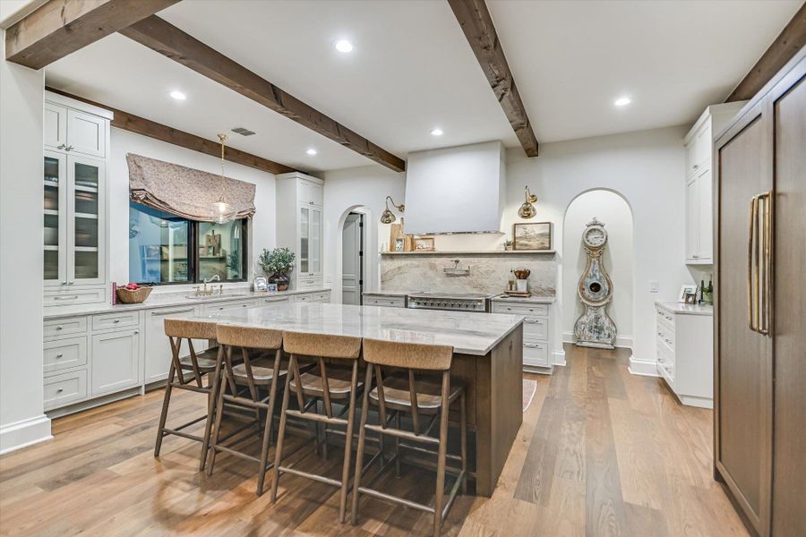 Kitchen featuring arched walkways, white cabinetry, glass insert cabinets, light stone counters, and a kitchen island Kitchen featuring arched walkways, white cabinetry, glass insert cabinets, light stone counters, and a kitchen island