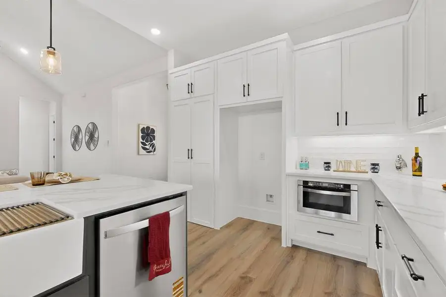 Kitchen with light stone countertops, stainless steel appliances, light wood-type flooring, decorative light fixtures, and white cabinetry