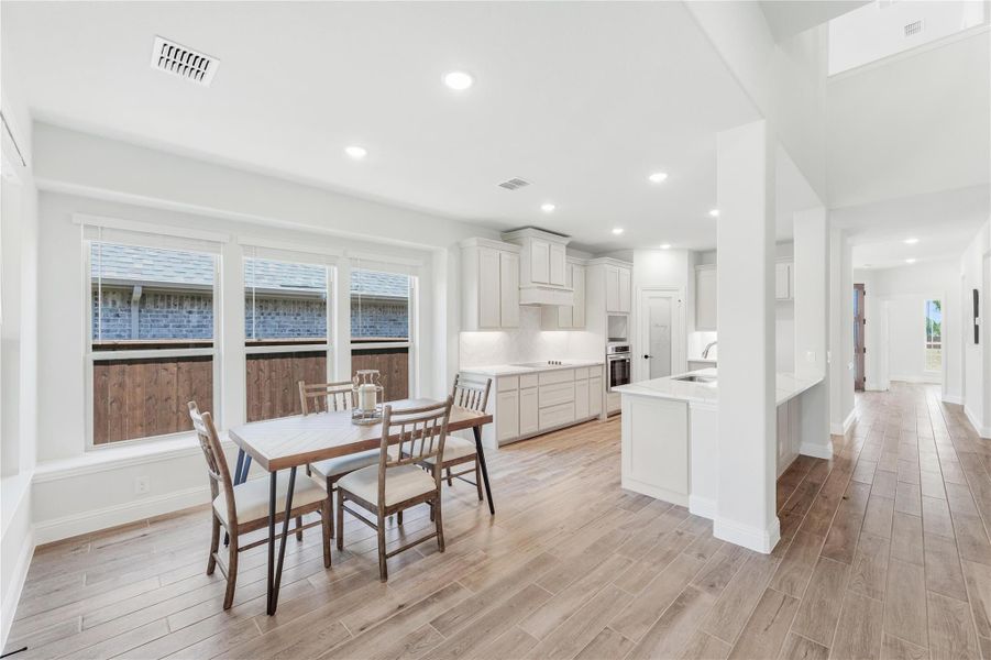 Open-concept dining area and kitchen with white cabinets, wood-look floors, and a four-seat dining table near large windows Open-concept dining area and kitchen with white cabinets, wood-look floors, and a four-seat dining table near large windows