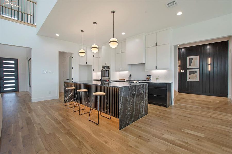 Kitchen featuring light wood-type flooring, stainless steel double oven, white cabinetry, pendant lighting, and a center island with sink