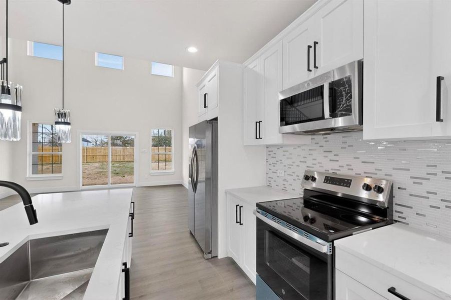 Kitchen featuring stainless steel appliances, hanging light fixtures, white cabinetry, light stone counters, and backsplash Kitchen featuring stainless steel appliances, hanging light fixtures, white cabinetry, light stone counters, and backsplash